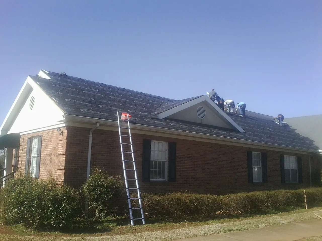 Crew tearing shingles off a brick ranch roof with a ladder set — Emergency Roof Repair work by our crew in Harrogate
