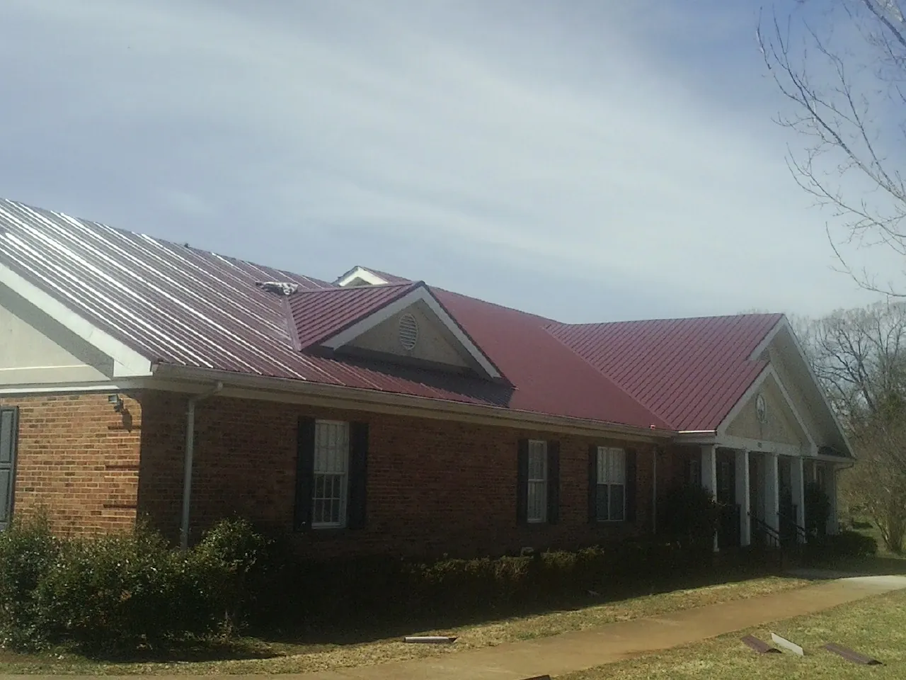 Red metal roof with gabled entries on a long brick building, from a Hail Damage Roof Repair job in Harrogate